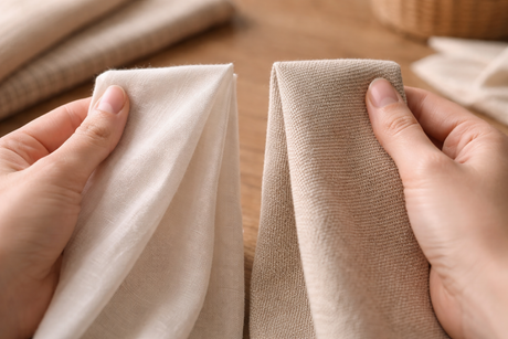 Hands comparing lightweight and heavier fabric samples to demonstrate differences in fabric weight.