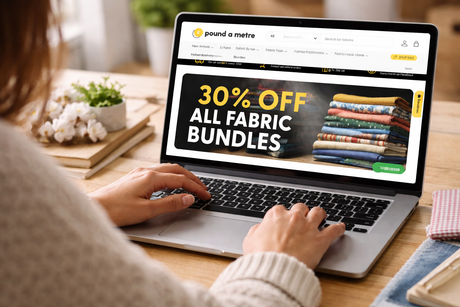 Woman browsing the Pound A Metre fabric website on a laptop, hands visible on the keyboard while viewing fabric bundles and offers