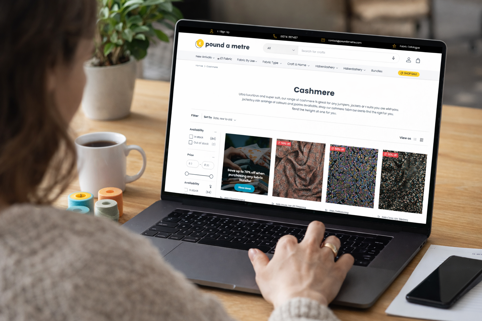 Woman browsing the Pound A Metre cashmere fabric collection on a laptop, viewing fabric options and preparing to choose materials