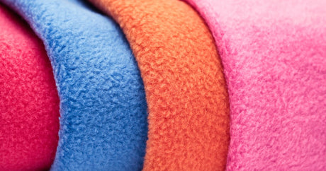 Close-up of folded polar fleece fabric in red, blue, orange and pink, showing the brushed pile