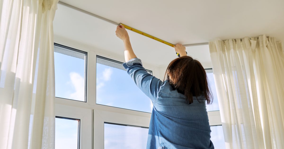 Woman measuring a curtain track with a tape measure before buying curtain fabric