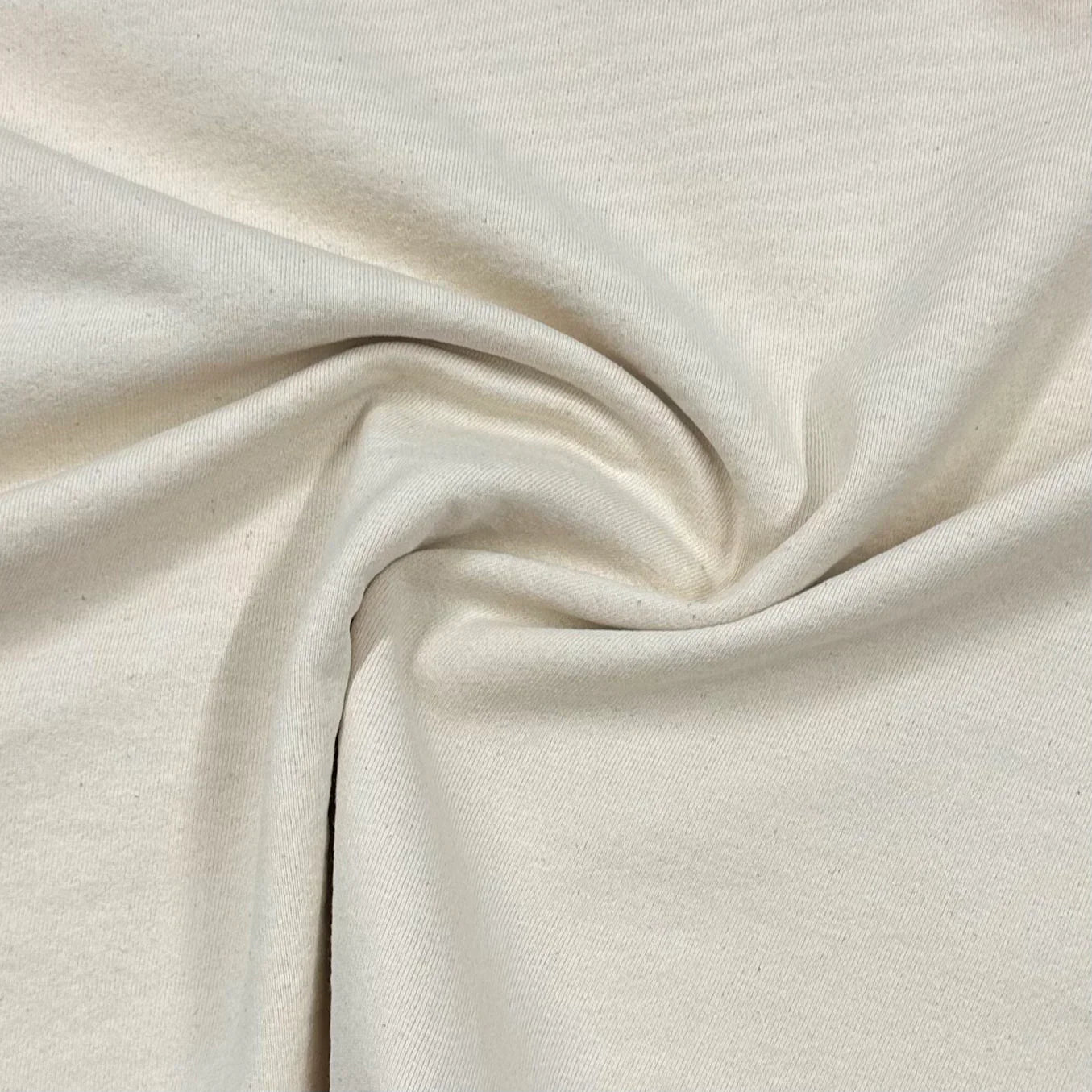 Plain fabric folded on a wooden table in natural light, showing colour depth and fabric texture.