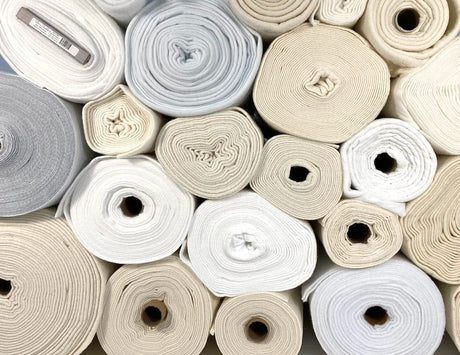 Collection of rolls of fabric in various neutral colors.